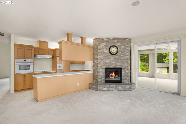 23705 SW Everest Ct, Sherwood, OR 97140 - kitchen featuring white oven, light carpet, under cabinet range hood, a brick fireplace, and a peninsula