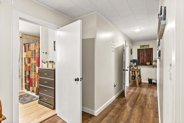 corridor featuring dark wood-style flooring, ornamental molding, and baseboards