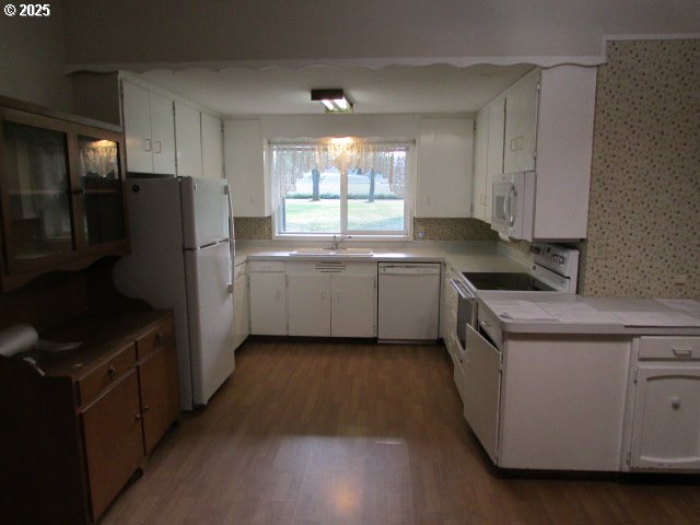 21451 SE Webfoot Rd, Dayton, OR 97114 - kitchen with white appliances, a sink, wood finished floors, white cabinets, and wallpapered walls