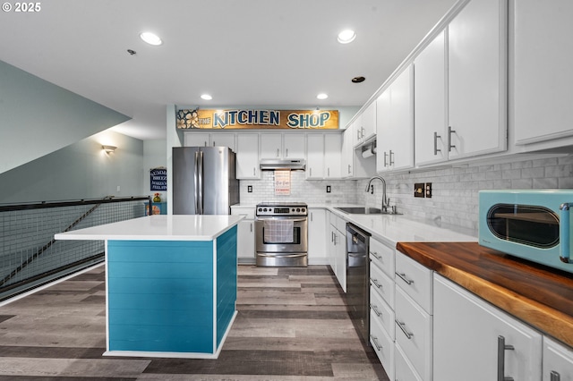 kitchen with a sink, stainless steel appliances, under cabinet range hood, and dark wood finished floors