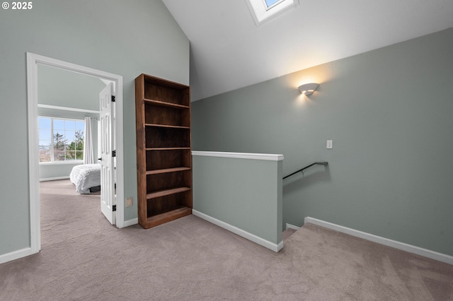 hallway with an upstairs landing, a skylight, baseboards, and carpet floors