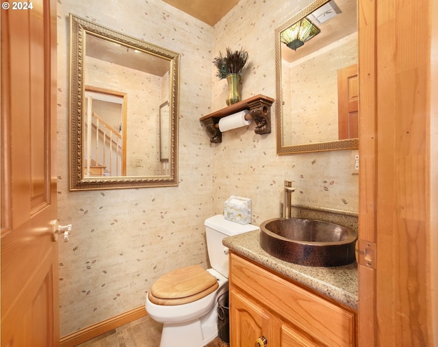 half bathroom featuring wallpapered walls, toilet, vanity, and baseboards