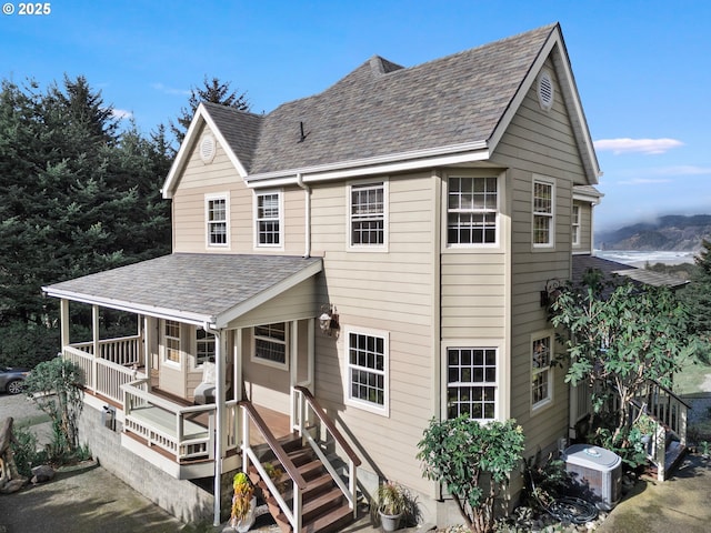 view of front facade featuring central air condition unit, covered porch, and roof with shingles