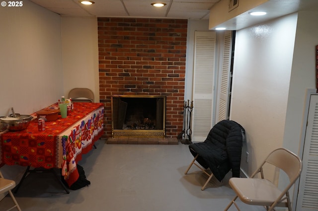 interior space featuring a brick fireplace, a paneled ceiling, and concrete flooring