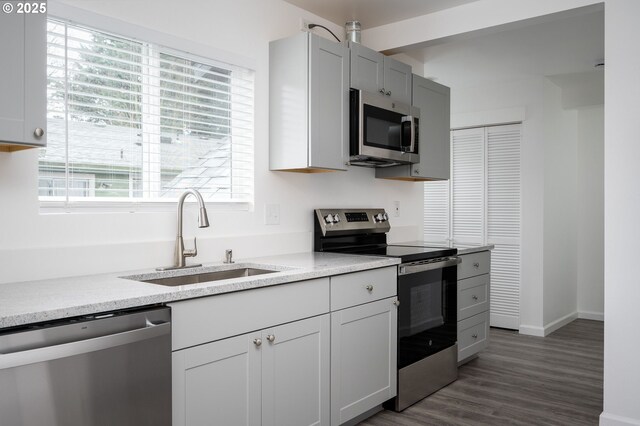 10304 SE Yukon St, Portland, OR 97266 - kitchen with appliances with stainless steel finishes, a sink, dark wood-style flooring, baseboards, and light stone counters
