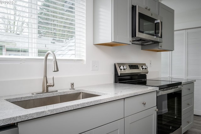 kitchen featuring light stone countertops, appliances with stainless steel finishes, sink, and gray cabinetry