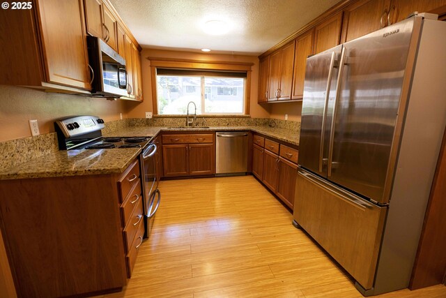 3663 Wilshire Ln, Eugene, OR 97405 - kitchen with appliances with stainless steel finishes, a sink, brown cabinets, light wood finished floors, and dark stone countertops