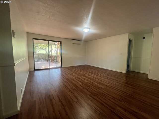 3663 Wilshire Ln, Eugene, OR 97405 - unfurnished room with a wall unit AC, dark wood finished floors, baseboards, and a textured ceiling