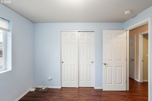 unfurnished bedroom with dark wood finished floors, a closet, and baseboards