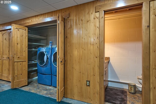 clothes washing area with laundry area, wood walls, washer and dryer, and concrete block wall