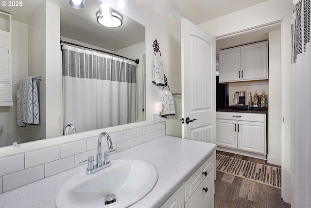 bathroom with vanity, a shower with shower curtain, wood finished floors, and backsplash