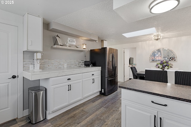 kitchen featuring tasteful backsplash, a skylight, freestanding refrigerator, dark wood-style floors, and white cabinets