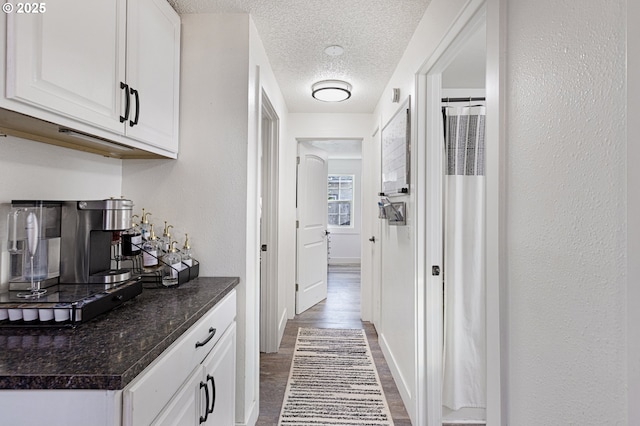 hallway featuring baseboards, a textured wall, dark wood-style flooring, and a textured ceiling