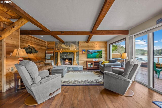 70202 Potato Bottom Rd, Lakeside, OR 97449 - living room featuring wood walls, beamed ceiling, hardwood / wood-style floors, a textured ceiling, and a fireplace