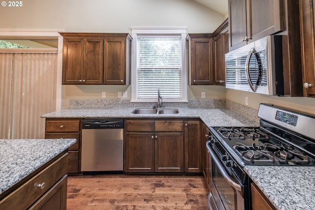 kitchen with light stone counters, wood finished floors, vaulted ceiling, stainless steel appliances, and a sink