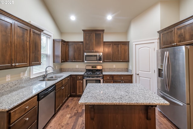 kitchen with lofted ceiling, a sink, appliances with stainless steel finishes, a center island, and dark wood-style floors