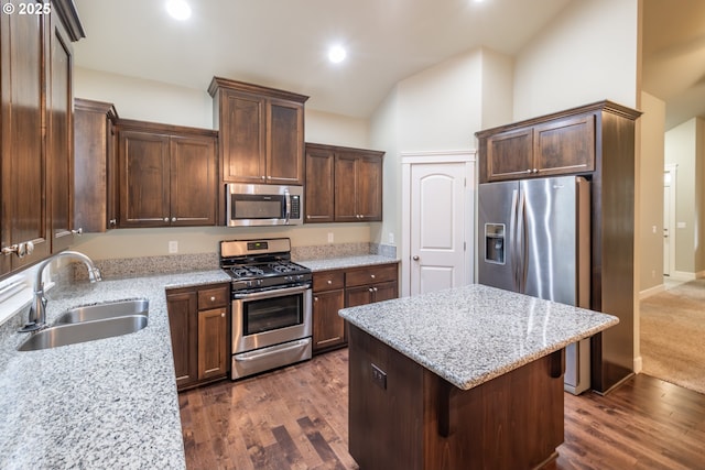 kitchen featuring dark wood-style flooring, a kitchen island, a sink, vaulted ceiling, and appliances with stainless steel finishes