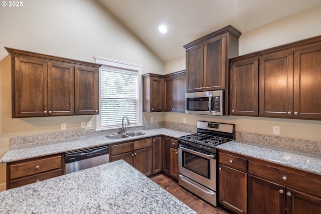 kitchen featuring lofted ceiling, appliances with stainless steel finishes, dark wood-style flooring, light stone countertops, and a sink