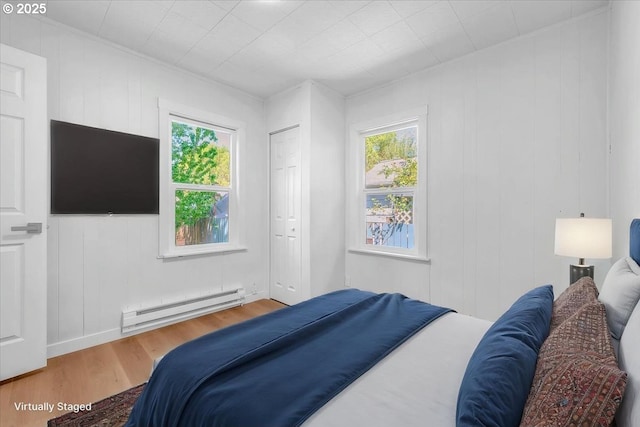 bedroom with a baseboard heating unit, multiple windows, and wood finished floors