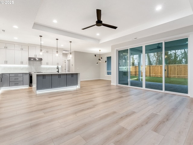 unfurnished living room featuring a raised ceiling, ceiling fan, sink, and light hardwood / wood-style floors