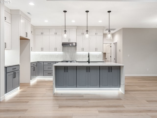 kitchen with pendant lighting, sink, gray cabinets, and a center island with sink