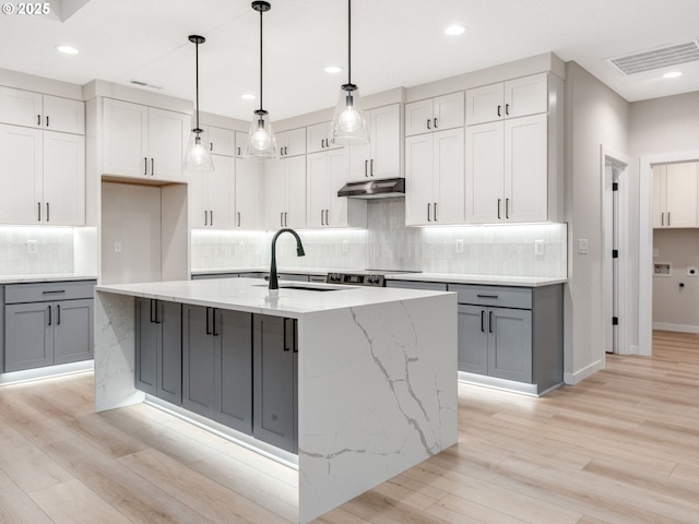 kitchen with visible vents, an island with sink, decorative light fixtures, light stone countertops, and under cabinet range hood