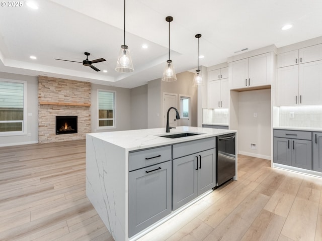 kitchen featuring sink, light stone counters, decorative light fixtures, a raised ceiling, and an island with sink