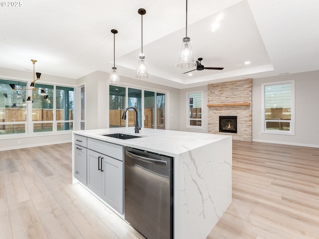 kitchen with pendant lighting, sink, light stone counters, a center island with sink, and stainless steel dishwasher