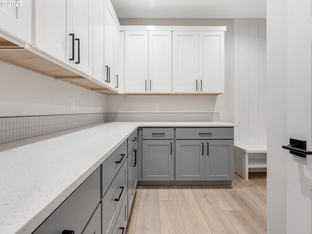 kitchen with light wood-type flooring, gray cabinets, white cabinetry, and light stone countertops