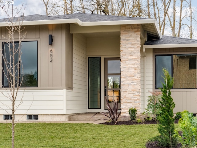 property entrance featuring a shingled roof, stone siding, and a lawn