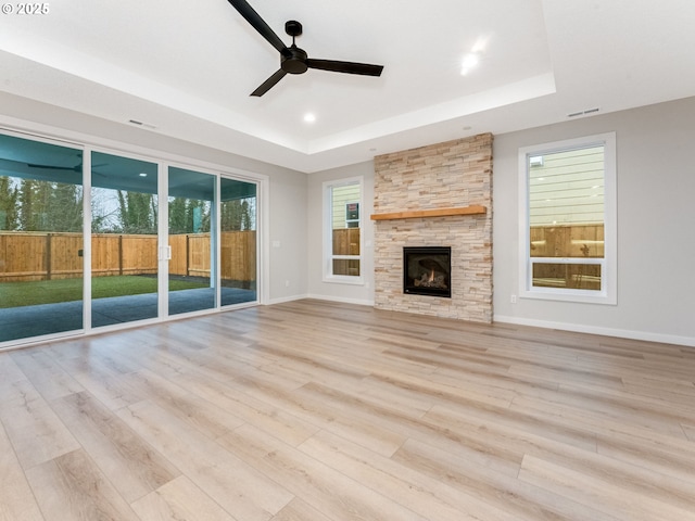 unfurnished living room with a fireplace, light wood-type flooring, a raised ceiling, and baseboards