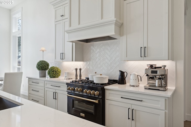 kitchen featuring premium range hood, high end stove, white cabinetry, decorative backsplash, and light stone countertops