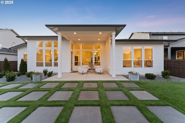 back house at dusk featuring a patio area and a lawn