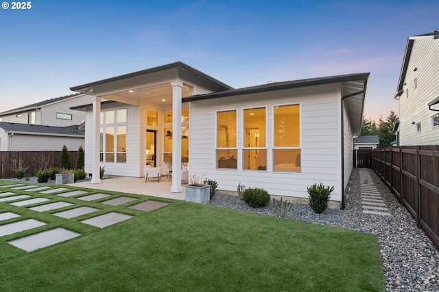 back house at dusk with a yard and a patio area