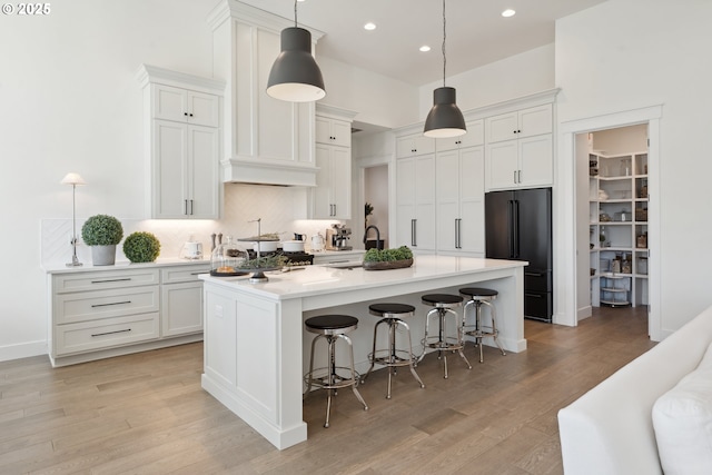 kitchen featuring a breakfast bar, white cabinetry, high quality fridge, a center island with sink, and decorative light fixtures