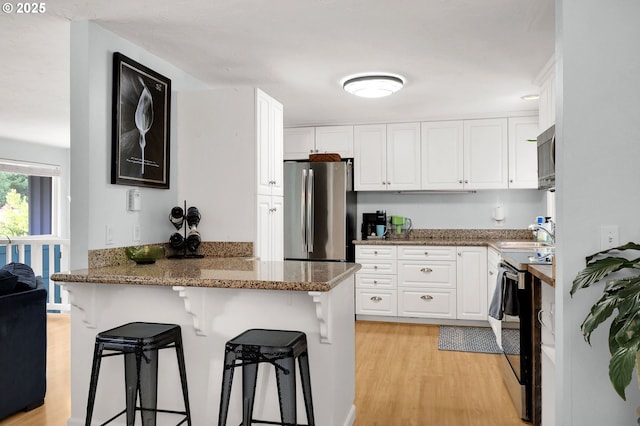 3580 Wilshire Ln, Eugene, OR 97405 - kitchen featuring stainless steel appliances, a peninsula, white cabinets, a breakfast bar area, and light wood-type flooring