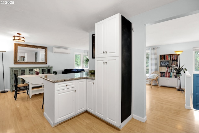 3580 Wilshire Ln, Eugene, OR 97405 - kitchen with a wall unit AC, light wood finished floors, white cabinets, and a peninsula