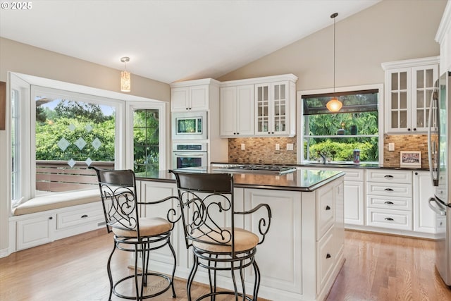 515 SW Colony Dr, Portland, OR 97219 - kitchen with dark countertops, appliances with stainless steel finishes, a center island, vaulted ceiling, and light wood finished floors