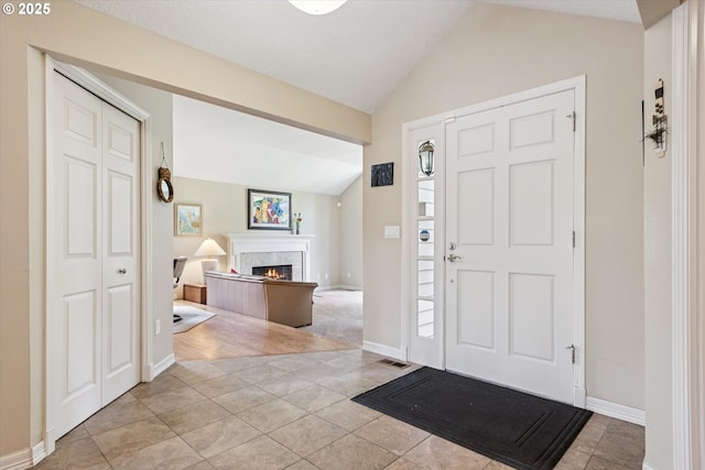 515 SW Colony Dr, Portland, OR 97219 - foyer entrance featuring vaulted ceiling, light tile patterned floors, a warm lit fireplace, and baseboards
