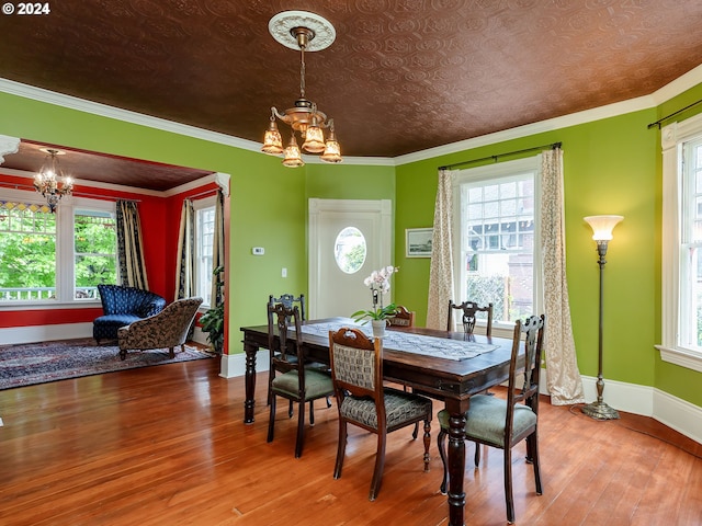 dining space with a wealth of natural light, crown molding, hardwood / wood-style floors, and an inviting chandelier