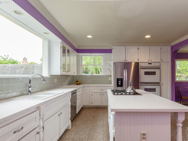 kitchen featuring appliances with stainless steel finishes, tasteful backsplash, sink, white cabinets, and a center island