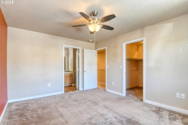 unfurnished bedroom featuring a walk in closet, light colored carpet, a closet, and a textured ceiling