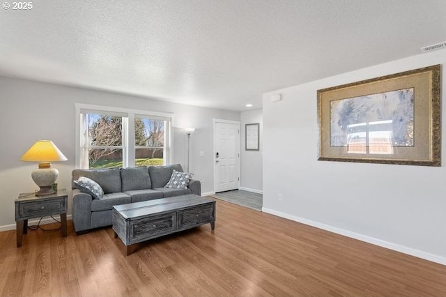 living area featuring visible vents, a textured ceiling, baseboards, and wood finished floors