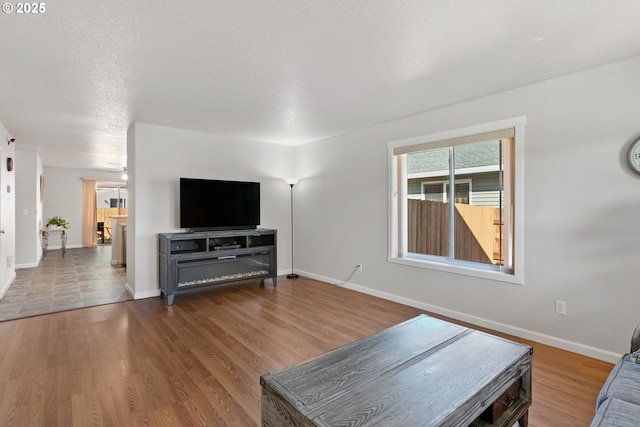 living area featuring a textured ceiling, wood finished floors, and baseboards