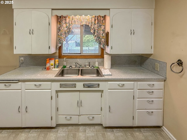 kitchen with white cabinets, baseboards, light countertops, and a sink