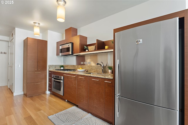 kitchen featuring stainless steel appliances, a sink, light wood-style floors, open shelves, and brown cabinetry