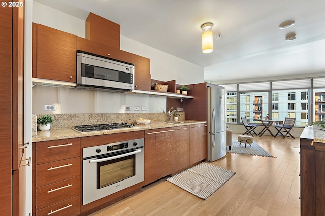 kitchen featuring brown cabinets, light wood finished floors, open shelves, stainless steel appliances, and a sink