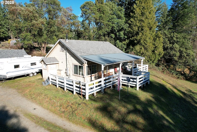 rear view of property featuring roof with shingles, a yard, a wooden deck, and view of scattered trees