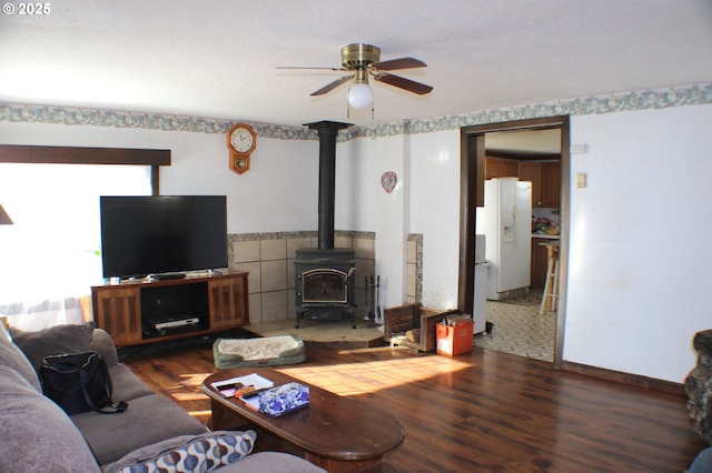 living room featuring wood-type flooring, ceiling fan, and a wood stove