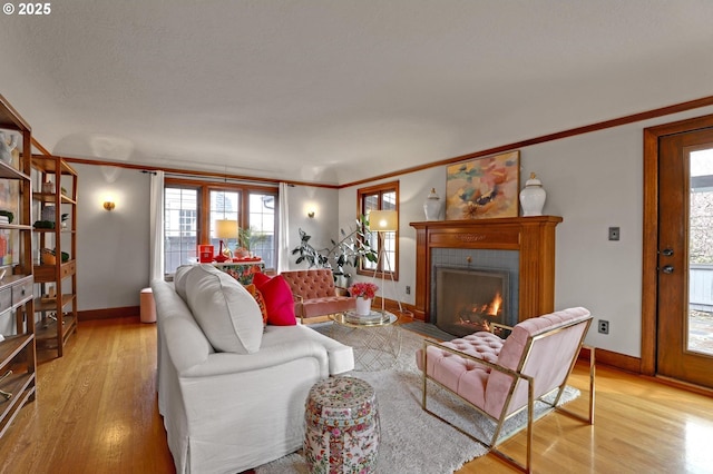 living area with a fireplace, crown molding, light wood-style floors, and baseboards